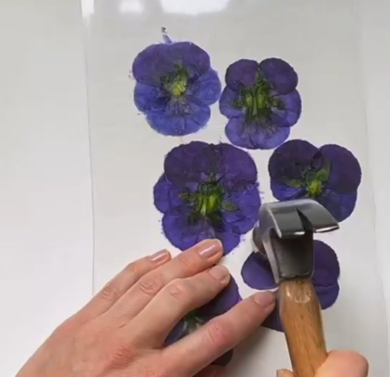 hands hammering purple petunias onto paper