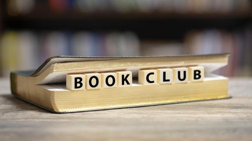 A book on a table with the words Book Club spelled out by blocks set inside its pages.