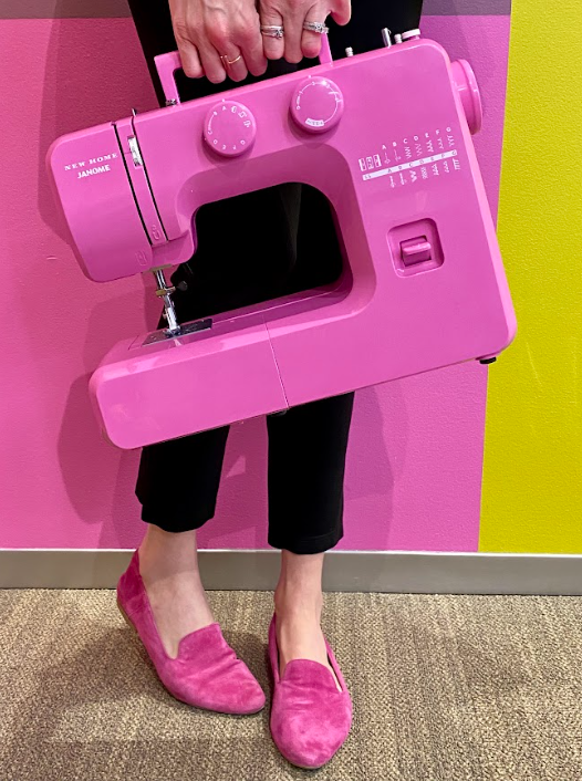 An image of someone holding a pink sewing machine with matching pink shoes 